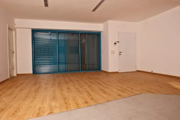 חלל עם רצפת עץ, קירות לבנים וויטרינה עם תריס כחול