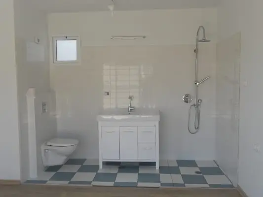 חדר רחצה עם ארון כיור לבן, אסלה תלויה, מקלחת ורצפה משובצת